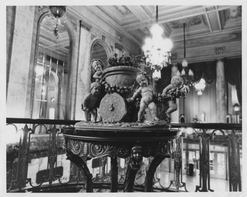 View overlooking the lobby from the mezzanine at the west end showing enormous arched window, coffered ceilings, original furniture, sculpture, and lighting fixtures.